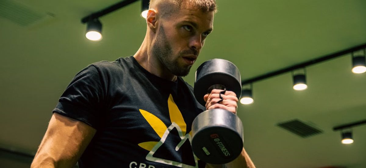 Muscular man exercising with a dumbbell in a modern gym setting, emphasizing strength and fitness.